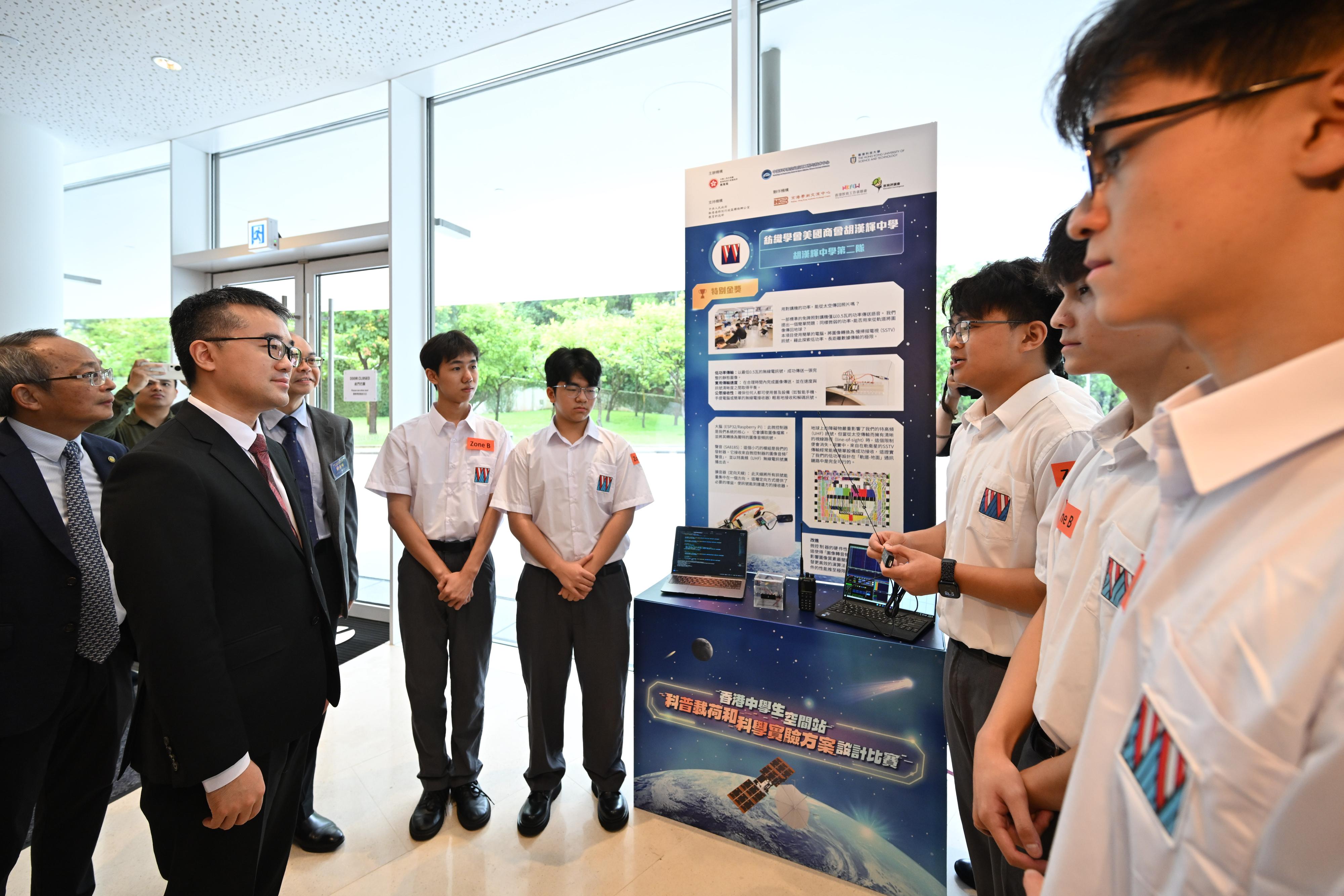 教育局在科大举办香港中学生空间站科普载荷和科学实验方案设计比赛颁奖典礼。图示科大副校长（研究及发展）郑光廷教授（左一）和教育局副局长施俊辉博士（左二）听取特别金奖队伍——纺织学会美国商会胡汉辉中学第二队学生介绍作品。